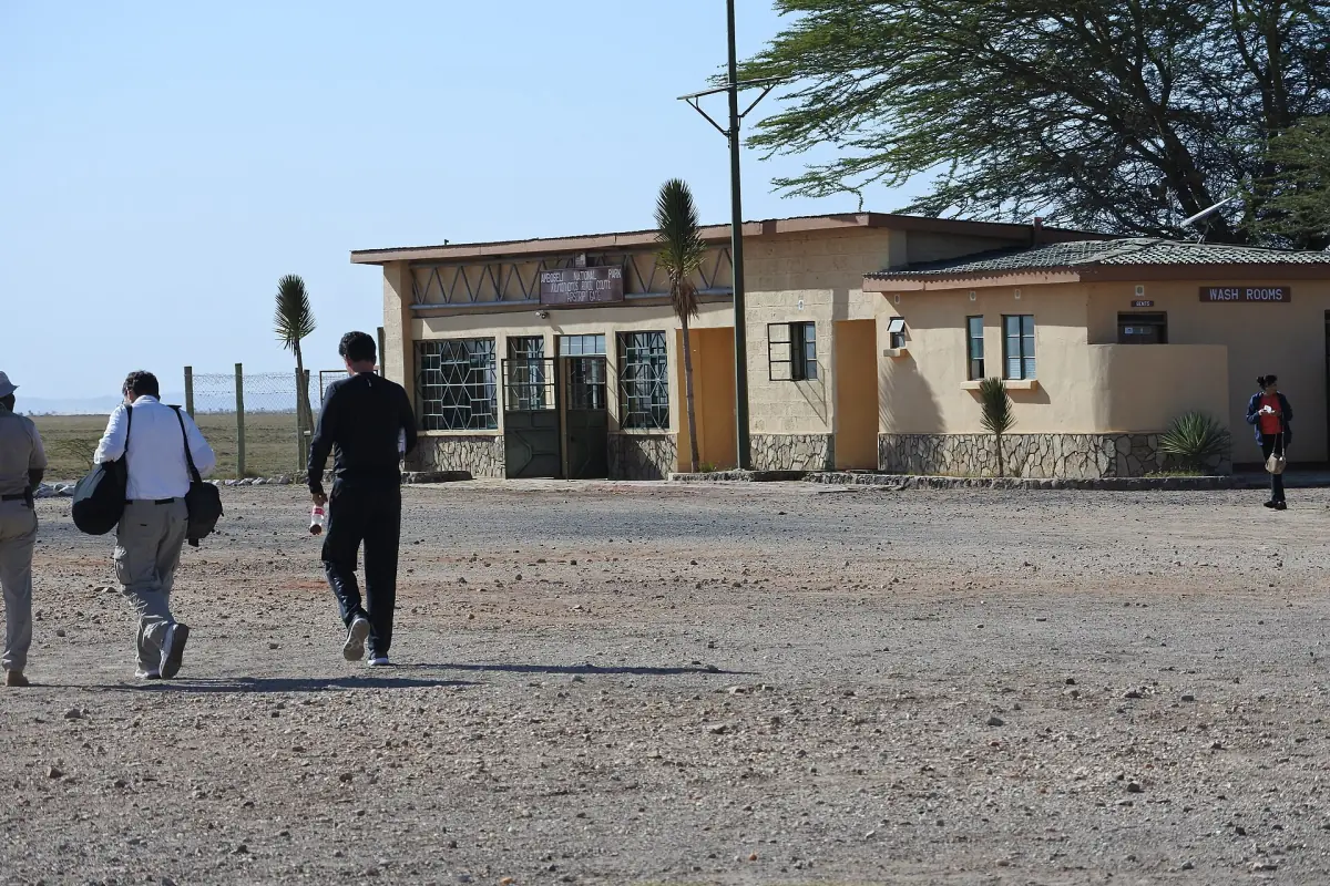 Airstrip terminal building with travellers walking across gravel in sunshine