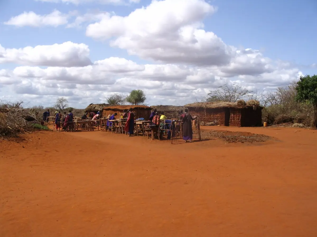 Maasai village with low huts and red earth under a cloudy blue sky