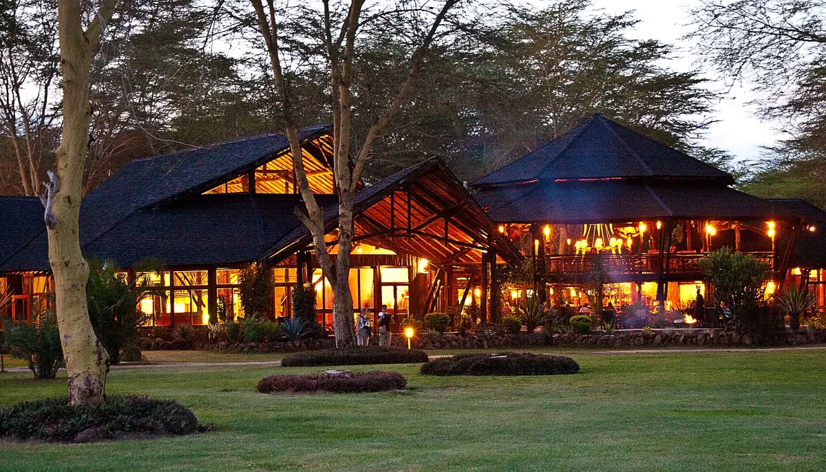 A lodge at Ol Tukai with lit windows and lawn at dusk