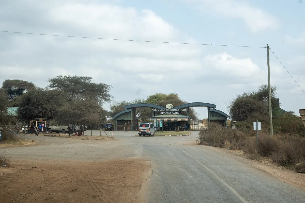 Paved road leading to the green Kimana Gate under a bright sky